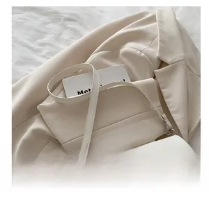 Detail of white leather shoulder bag featuring a wide strap and large silver square buckle
