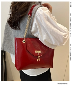 Detail of red patent leather tote bag with gold deer charm and chain strap