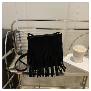 Close-up of black fringe tassel crossbody bag on a modern minimalist display rack