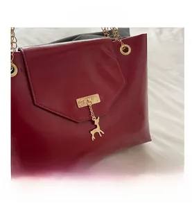 Detail of dark red patent leather tote with gold deer pendant and metal chain strap
