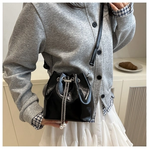 Detail der schwarzen glänzenden Beuteltasche mit silberner Kette und Perlenakzent