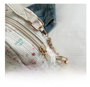 Detail of golden metal zipper and chain strap on a white floral quilted crossbody bag