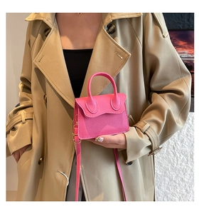 Détail d'un sac à main rose grainé avec boucle dorée porté sur un manteau kaki