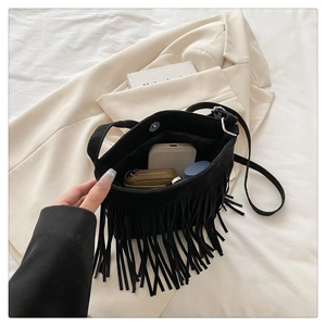 Detail of black suede fringe crossbody bag with metal buckle on beige blazer background