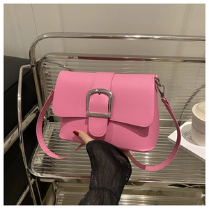 Close-up of pink crossbody bag with large silver buckle on smooth faux leather surface