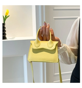 Détail d'un mini sac à main jaune vif en cuir grainé tenu à la main sur fond blanc