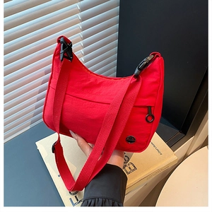 Detail of red nylon crescent crossbody bag with black buckle and metal M logo plaque