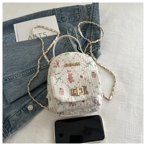 Detail of white mini backpack with floral bear prints and metal chain strap on flat lay