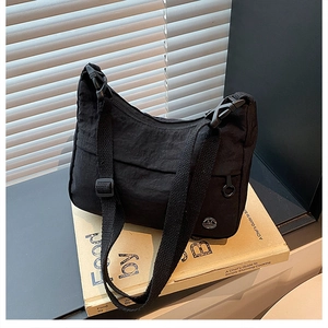 Detail of minimalist black nylon crossbody bag with adjustable strap and logo on prop books