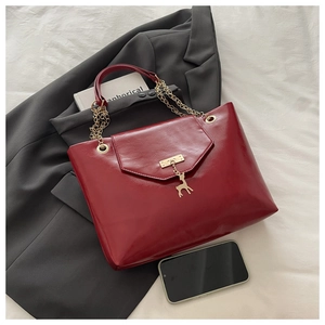 Detail of red glossy handbag featuring a gold deer charm and elegant chain strap
