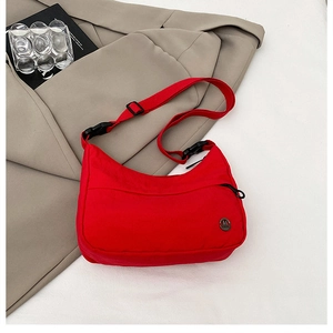 Close-up of red nylon crossbody bag with metal M logo on khaki blazer background