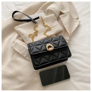 Detail of black quilted shoulder bag with gold horseshoe lock and chain strap next to a phone