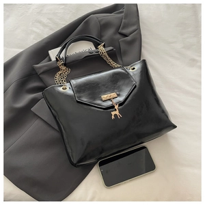 Detail of black glossy tote bag with gold chain strap and deer charm on a suit