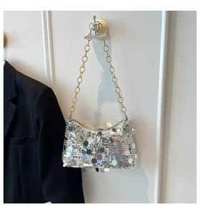 Détail du sac croissant à paillettes argentées avec chaîne dorée sur mur blanc