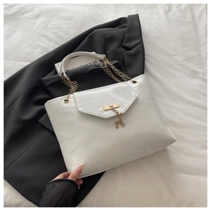 Close-up of white leather tote bag featuring gold deer pendant and chain strap detail