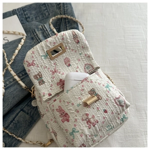Detail einer weiß gesteppten Mini-Umhängetasche mit rosa Motiven und Kettenriemen