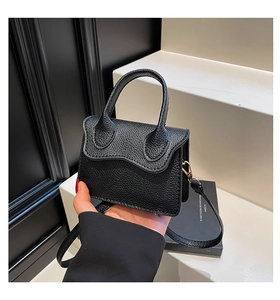 Detail of black mini handbag with lychee pattern texture and scalloped flap design