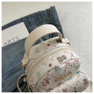 Detail eines weißen Mini-Rucksacks mit Blumen-Bären-Print und goldenem Logo