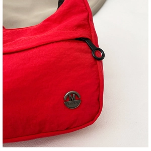 Close-up of red nylon bag featuring a silver M FASHION metal logo and black zipper detail