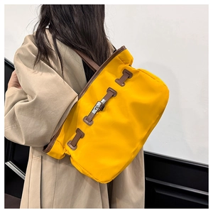 Détail du sac cabas en nylon jaune avec bordure en cuir et serrure sur un trench-coat kaki