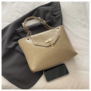 Detail of beige tote bag with chunky gold chain strap and deer charm on a grey blazer
