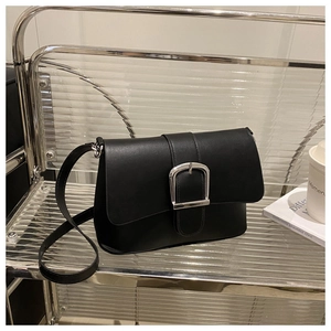 Close-up of a black leather square bag featuring a silver horseshoe buckle on a glass shelf