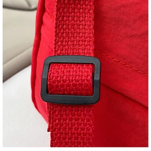 Close-up of red nylon fabric texture and black plastic strap adjuster on crossbody bag