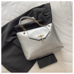 Detail of silver tote bag with golden deer charm and metallic chain handle next to phone