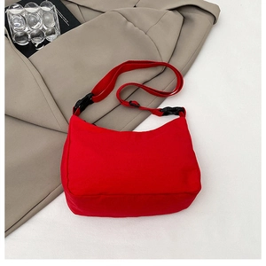 Detail view of a bright red nylon crossbody bag with black adjustable strap on white surface