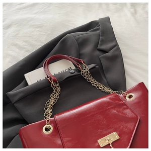 Detail of dark red tote bag with glossy leather texture and gold chain handle