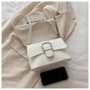 Detail of white leather shoulder bag with silver buckle on beige blazer background