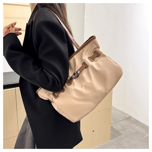 Détail d'un grand sac bandoulière beige et marron sur un mannequin portant une veste noire