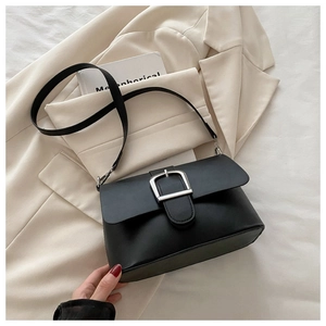 Detailed view of matte black leather handbag with a large silver buckle on a beige blazer
