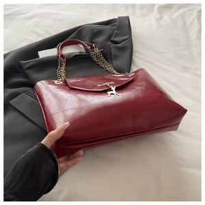 Close-up of wine red glossy leather tote bag with golden chain and deer metal ornament