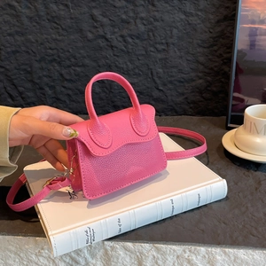 Mini sac à main fuchsia en cuir à grain lychee avec bandoulière sur un livre blanc