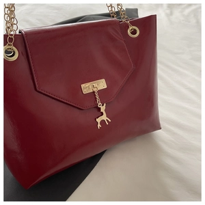 Detailed shot of red glossy tote bag featuring gold chain strap and deer charm