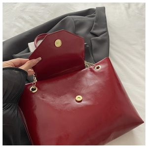 Close-up of deep red glossy tote bag with golden chain strap and magnetic flap closure