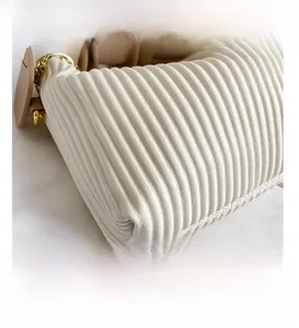 Macro view of vertical pleated texture on a cream handbag with gold metal chain link detail