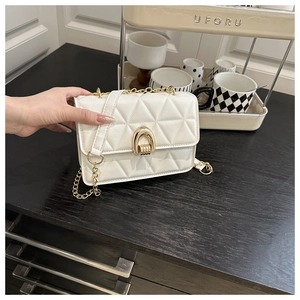 Close-up of white quilted crossbody bag featuring a gold horseshoe buckle and chain strap