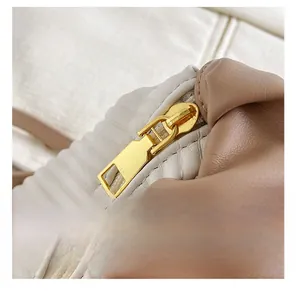 Close-up of smooth gold metal zipper on pleated cream and brown leather handbag