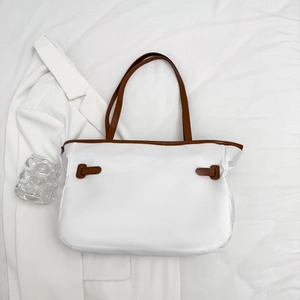 Sac cabas blanc minimaliste avec bordures marron et doubles anses sur un blazer blanc
