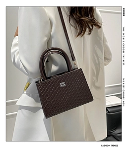 Detail of dark brown croc-effect leather handbag with metallic logo and top handles