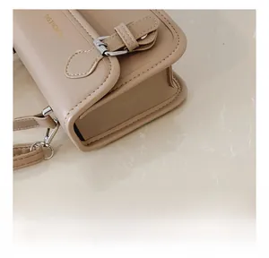Detailed view of the precise stitching and silver buckle on the beige leather crossbody bag