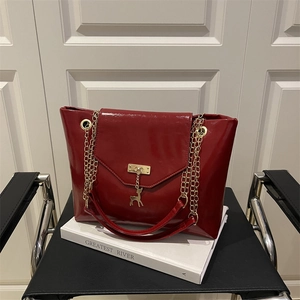 Red patent leather tote bag with gold chain straps and a deer charm on a book
