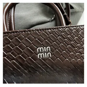 Detail of deep brown woven leather texture with a polished metallic brand logo plate