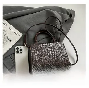 Detail of dark brown faux crocodile leather bag with metal logo on a grey blazer fabric