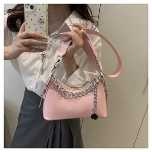 Detail of light pink crossbody bag with silver chain and wide leather strap held by a model