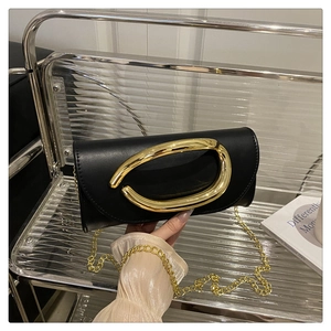Detailed view of black leather clutch bag with large gold C-handle and fine metal chain