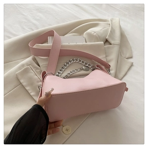 Pink niche handbag with silver metal chain handle and wide leather strap on beige blazer