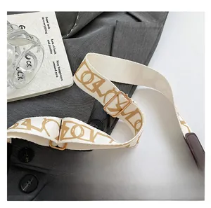 Detail of adjustable off-white woven shoulder strap with gold hardware and logo pattern